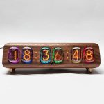 Relógio Nixie vintage com números coloridos em tubos de vidro, caixa de madeira escura e base de suporte de madeira clara.