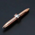 Caneta de metal com corpo dourado rosé, detalhes cromados, com botão para ativar LED na extremidade, sobre fundo preto.