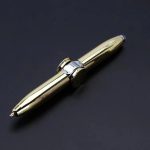 Caneta dourada com detalhes prateados, corpo metálico brilhante, em fundo preto, vista lateral, com tampa removida.