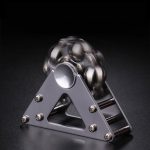 Spinner de mão com bolas metálicas em movimento, destaque para estrutura triangular de metal e bolas de aço brilhantes.