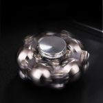 Spinner de mão com várias esferas metálicas brilhantes em movimento, focado no centro, sobre fundo escuro.