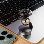 Anel de metal com anel de vidro colocado sobre o teclado de um portátil, com um smartphone ao lado.