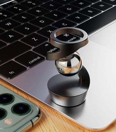 Anel de metal com anel de vidro colocado sobre o teclado de um portátil, com um smartphone ao lado.
