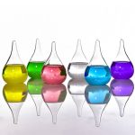 Seis frascos de vidro com líquidos de cores diferentes: amarelo, verde, rosa, transparente, azul e roxo, refletidos numa superfície brilhante.