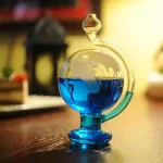 Termómetro de Galileu com esfera de vidro contendo líquido azul, colocado numa mesa de madeira com fundo desfocado de decoração de ciência.