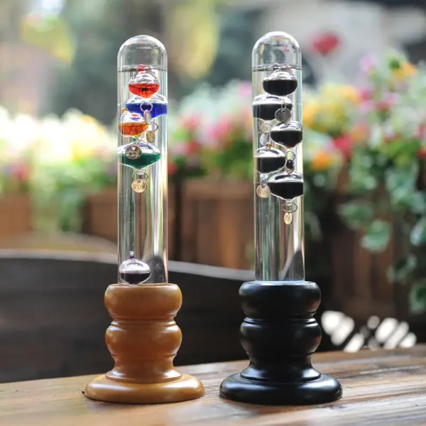 Dois termómetros de Galileu com esferas coloridas, um com esferas vermelhas e o outro com esferas pretas, colocados sobre uma mesa de madeira ao ar livre.