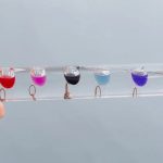 Vários líquidos coloridos em pequenos recipientes de vidro suspensos em uma linha, usados para demonstração de temperatura com o termómetro de Galileu.