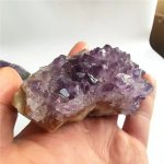 Ametista escura em bruto com cristais violetas, vista de perto na mão, detalhes das formações cristalinas e textura.