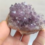 Ametista escura em bruto com cristais violetas, vista de perto, mostrando detalhes das formações cristalinas.
