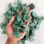 Pedras de aventurina bruta de vários tamanhos e formas, com tonalidades verdes, sobre fundo branco.