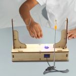 Mão de criança ajustando fios elétricos em suporte de madeira com lâmpada de plasma acesa, demonstrando circuito elétrico simples.