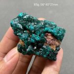 Cristal de Dioptase bruto com cor verde vibrante, textura cristalina e tamanho de 56x40x21mm, mostrado na mão para escala.