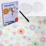 Espirógrafo transparente com várias rodas de diferentes tamanhos, acompanhado de um lápis preto e uma folha com desenhos coloridos de espirógrafos.