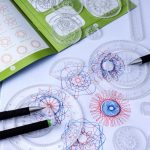 Conjunto de espirógrafos transparentes com desenhos coloridos feitos com canetas de diferentes cores, mostrando detalhes de padrões geométricos complexos.