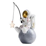Estatueta de um astronauta sentado na lua, segurando uma vara de pescar com uma estrela de madeira na ponta, com capacete dourado e mochila espacial.