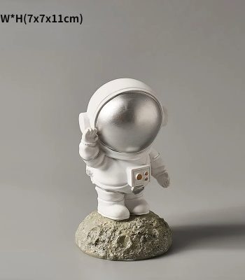 Estatueta de astronauta com capacete prateado, segurando uma caixa, colocada sobre uma base de rocha, com detalhes em branco e prateado.