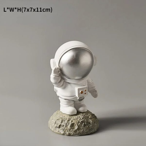 Estatueta de astronauta com capacete prateado, segurando uma caixa, colocada sobre uma base de rocha, com detalhes em branco e prateado.