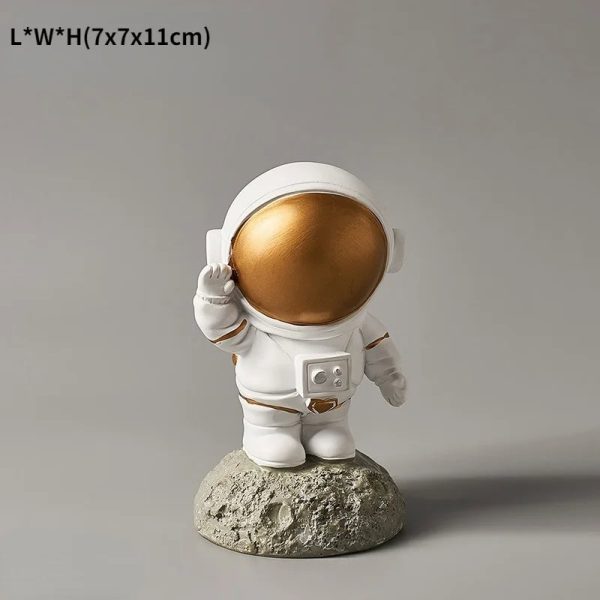 Estatueta de astronauta com capacete dourado, vestuário branco, em pé sobre uma base de rocha, com detalhes de capacete e traje espacial.
