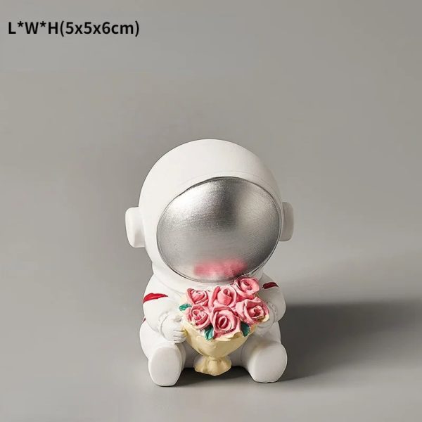Estatueta de astronauta com capacete prateado e corpo branco, segurando um ramo de rosas cor-de-rosa, em posição sentada.