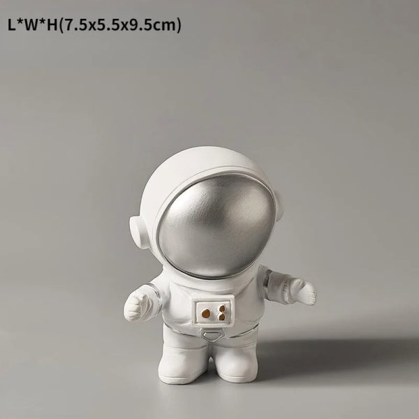 Estatueta de astronauta com capacete prateado e fato branco, com detalhes em cinza, de pé sobre fundo cinzento.