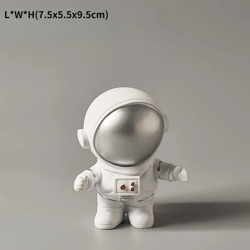Estatueta de Astronauta de Pé Estatueta de astronauta com capacete prateado e fato branco, com detalhes em cinza, de pé sobre fundo cinzento.