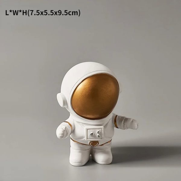 Estatueta de astronauta com capacete dourado, corpo branco e detalhes em dourado, em posição de pé com braços ligeiramente abertos.
