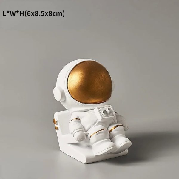 Estatueta de astronauta com capacete dourado e traje branco, sentado numa base, com detalhes em dourado e botões na roupa.
