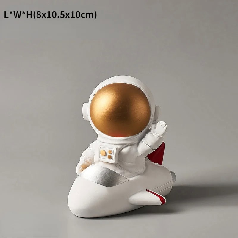 Estatueta de Astronauta em Foguetão Estatueta de astronauta com capacete dourado, sentado num foguete branco com detalhes vermelhos, em posição de descanso.