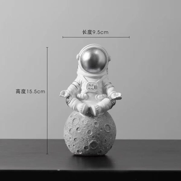 Estatueta de astronauta em posição de meditação, sentado sobre uma réplica da Lua com detalhes de crateras, em tom cinza e branco.
