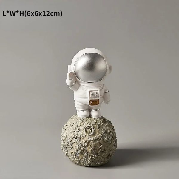 Estatueta de astronauta em traje espacial branco, de pé numa rocha lunar, com capacete prateado e detalhes em dourado na mochila.