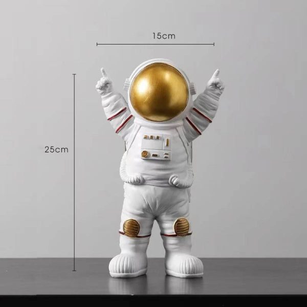 Estatueta de astronauta com capacete dourado, traje branco com detalhes vermelhos e acessórios em relevo, medindo 25cm de altura e 15cm de largura.
