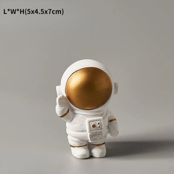 Miniatura de astronauta dourado com capacete grande, detalhes em branco e uma mochila de suporte, em pose de saudação.