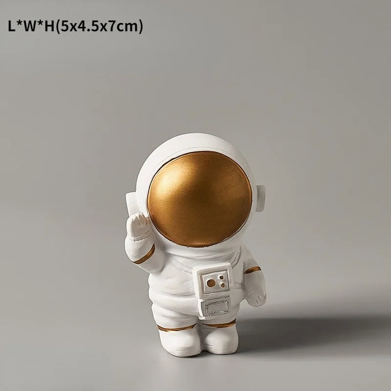 Estatueta Astronauta Dourada Pequena Miniatura de astronauta dourado com capacete grande, detalhes em branco e uma mochila de suporte, em pose de saudação.