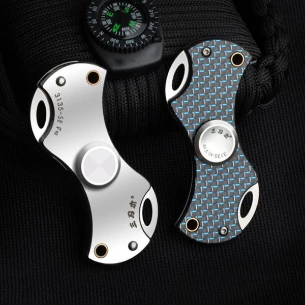 Faca de escalada com lâmina de metal escovado, detalhes em azul e branco, e orifícios para peso reduzido, presa a uma mochila de tecido preto.