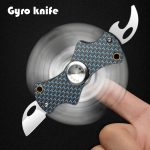 Faca Gyro Spin com lâmina de fogo, corpo de metal com padrão azul e detalhes dourados, em movimento, com dedo a segurar.