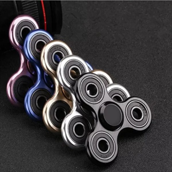 Conjunto de cinco fidget spinners em cores metálicas, com diferentes acabamentos, colocados sobre uma superfície escura.