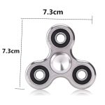 Fidget spinner de metal com três braços, cada um com rolamentos visíveis, medindo 7.3cm de diâmetro, usado para aliviar o stress.