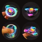 Fidget spinner de metal com acabamento brilhante, capturado de vários ângulos, mostrando o movimento e o efeito de luzes coloridas na superfície.