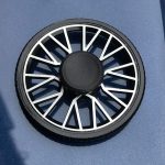 Fidget spinner com design de roda, com raios brancos e centro preto, colocado sobre uma superfície azul escura.