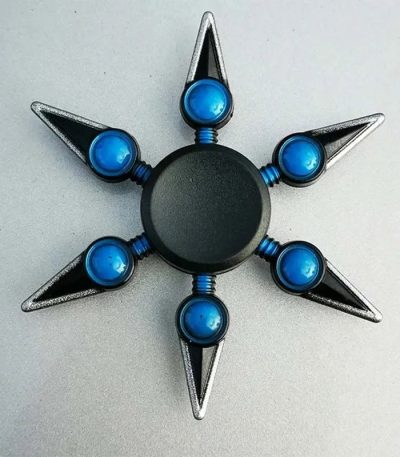 Fidget spinner com formato de kunai, com lâminas metálicas e detalhes azuis, visto de cima.