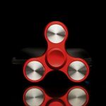 Fidget spinner vermelho com três braços, cada um com uma rotação metálica, sobre fundo preto.