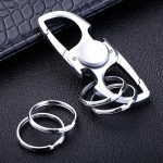 Chaveiro com design de porta-chaves em forma de fidget spinner de metal, com detalhes em prata e uma argola para chaves.