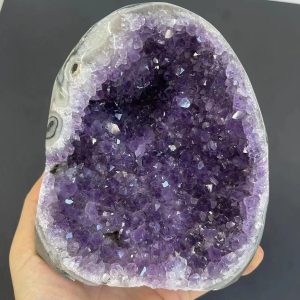 Geodo de ametista aberto mostrando cristais violeta brilhantes e bem formados, com uma camada exterior cinzenta e lisa.
