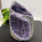 Geodo de ametista aberto mostrando cristais roxos brilhantes e estrutura cristalina interna, com detalhes de escamas e tonalidades variadas de roxo.