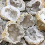 Vários geodos de cristal de rocha abertos, mostrando cristais de quartzo branco e transparente no interior, com bordas irregulares e textura áspera na parte exterior.