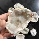 Geodo de cristal de rocha com interior cristalino, visto de perto, com várias peças ao fundo.