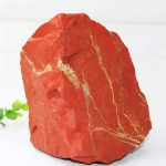 Jaspe vermelho bruto com veios dourados e textura irregular, destaque para a superfície áspera e cores vibrantes.