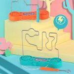 Circuito de jogo de destreza com fios de metal, componentes coloridos e painel de controle, em ambiente colorido com escadas e decoração temática.