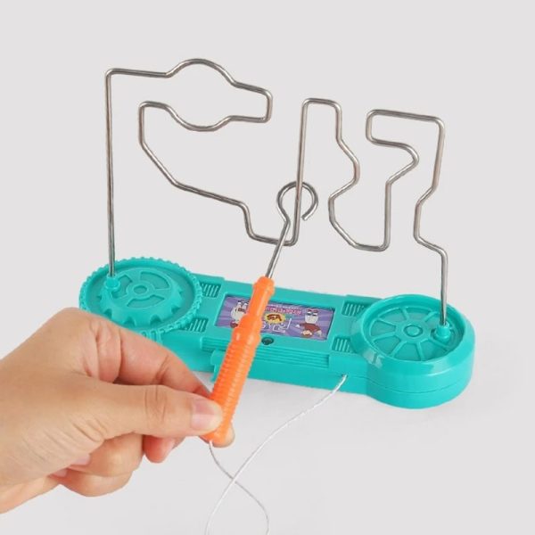 Mão segurando uma ferramenta de metal com uma ponta de plástico laranja, manipulando um circuito elétrico em um jogo de destreza com componentes de plástico azul e fios finos.