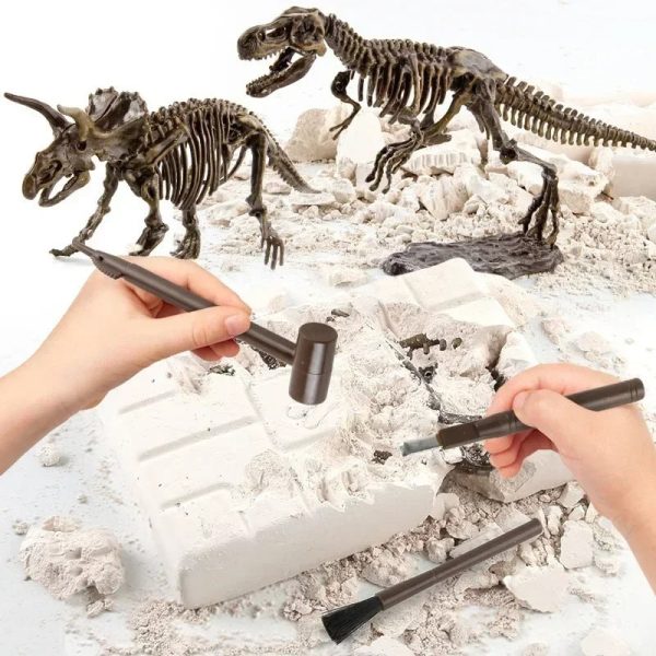 Duas mãos a usar ferramentas de escavação em uma caixa de areia com fósseis de dinossauros e esqueletos de dinossauros ao fundo.
